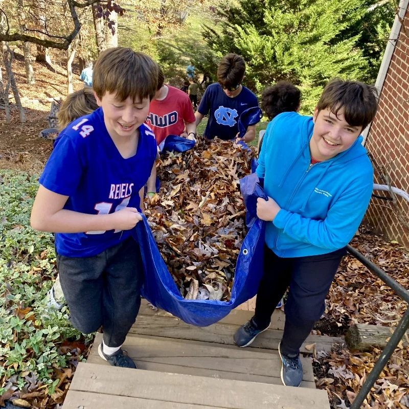 students carrying a tarp full of leaves up the stairs