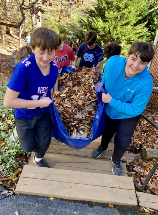 Students carrying a tarp full of leaves for a Rake-A-Thon